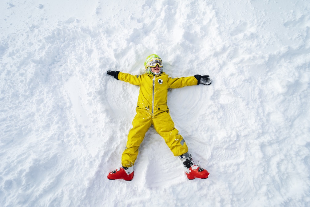 Bambino fa un angelo sulla neve su una distesa innevata.