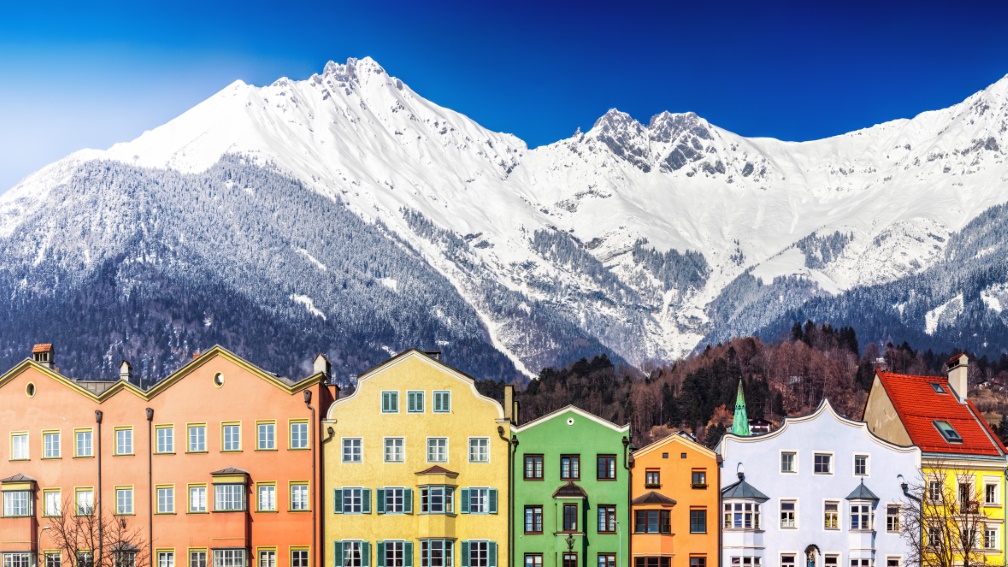 Bunte Häuser vor schneebedecktem Bergpanorama.